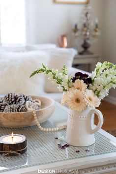 a table topped with a white vase filled with flowers next to a bowl of pine cones