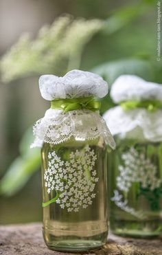 two mason jars with white flowers in them on a tree stump, one is decorated with lace and the other is filled with baby's breath