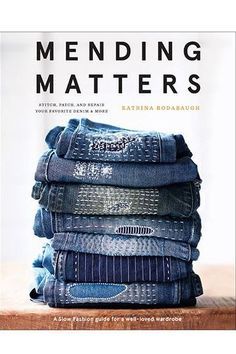 a stack of folded jeans sitting on top of a wooden table next to a book cover