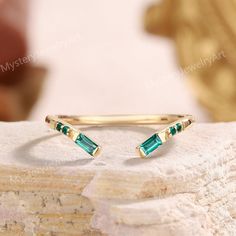 a gold ring with two green stones on it sitting on top of a white rock