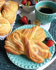 two blue plates topped with pastries next to cups of coffee and strawberries on a table