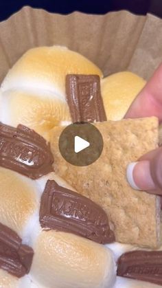 a person holding a piece of food in front of a bowl filled with bread and marshmallows