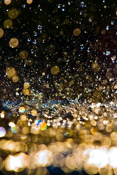 rain drops falling down on the ground and onto the water with blurry lights in the background