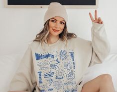 a woman sitting on top of a bed wearing a white sweatshirt and beanie hat