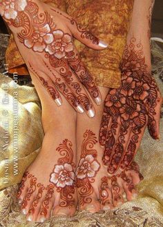 two women with henna tattoos on their hands and feet, one is holding the other's hand