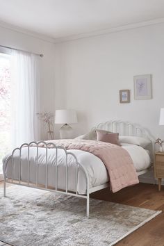 a white bed sitting in a bedroom on top of a wooden floor next to a window