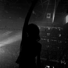 a woman standing in front of a crowd at a concert with her arm up to the sky