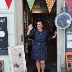 a woman is standing in front of the door to a cafe with her hand up