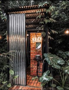 an outdoor shower in the middle of some plants and lights hanging from it's roof