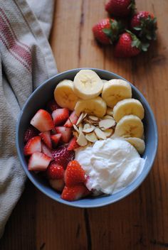 a bowl filled with fruit and yogurt on top of a wooden table next to strawberries