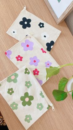 three flowered pouches sitting on top of a wooden table next to a potted plant