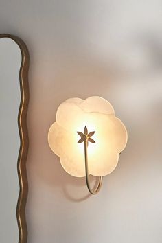 a light that is on the side of a wall next to a mirror with a flower in it