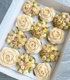 cupcakes decorated with white frosting and flowers on top of each other in a box