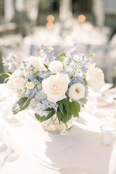 a vase filled with white and blue flowers sitting on top of a table next to candles