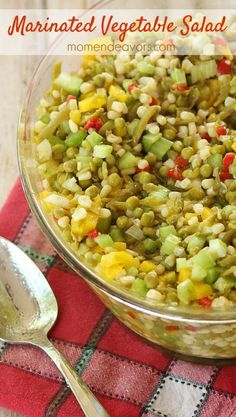 a glass bowl filled with mixed vegetables on top of a red and white checkered table cloth