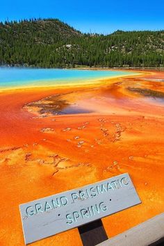 a sign that reads grand prismatic spring in front of a lake with orange and blue water