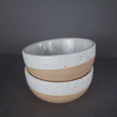 two white bowls with speckles are stacked on top of each other in front of a gray background