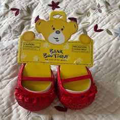 a pair of red shoes sitting on top of a bed next to a teddy bear