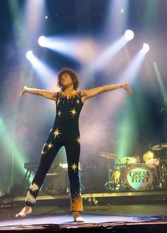 a man standing on top of a stage with his arms outstretched in the air and lights behind him