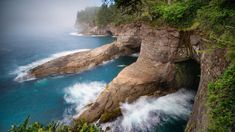 an ocean cliff with waves coming out of it and some trees on the other side