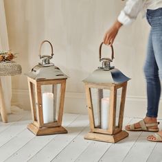 a woman standing next to two wooden lanterns with white candles in them on the floor