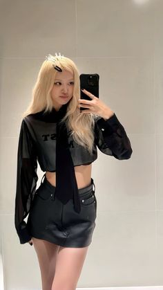 a woman taking a selfie in front of a mirror wearing a black shirt and leather skirt