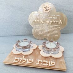 two candles sitting on top of a wooden tray next to a plaque with hebrew writing