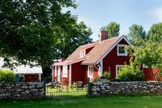 a red house sitting next to a stone wall and green grass covered yard with trees in the background