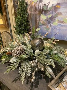 a christmas centerpiece with pine cones, greenery and balls on a wooden table