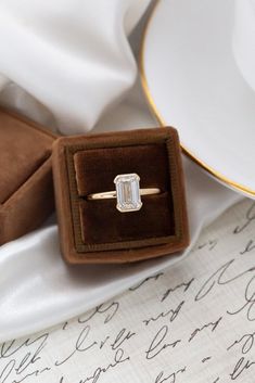 an engagement ring sitting in a velvet box on top of a white table cloth next to a cup and saucer