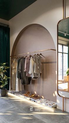 a clothing rack in front of a mirror with clothes hanging on it and a potted plant next to it