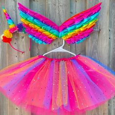 a dress made out of tulle and rainbow wings on a hanger next to a wooden fence