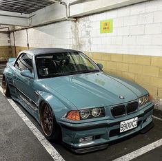 a blue car parked in a parking space next to a yellow brick wall with graffiti on it