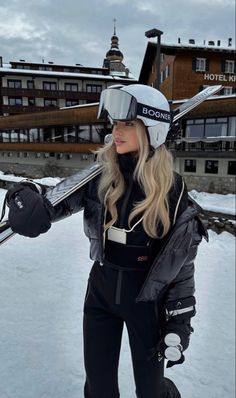 a woman holding skis in the snow with buildings in the background