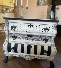 a white dresser with black and white designs on the drawers is sitting on a wooden floor