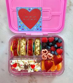 a pink lunch box filled with fruit and veggies on top of a table