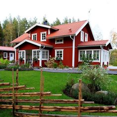 a red house sitting on top of a lush green field next to a wooden fence