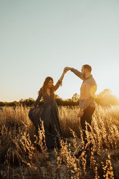 a man and woman dancing in the middle of a field with tall grass at sunset