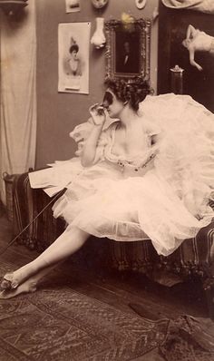 an old photo of a woman in a white dress sitting on a chair with her legs crossed