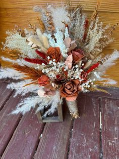 an arrangement of dried flowers and feathers on a wooden floor with wood planks in the background