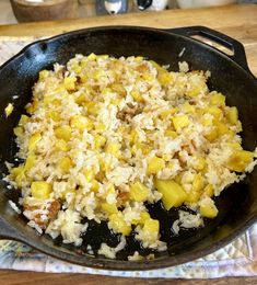 a skillet filled with rice and vegetables on top of a wooden table