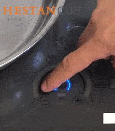 a person pressing the button on an electric stove with blue light coming from under it