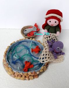 crocheted doll and fish in bowl on white surface with small pebbles around it