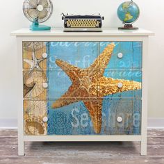 a white dresser with a starfish painted on the front and side drawers, along with a blue globe