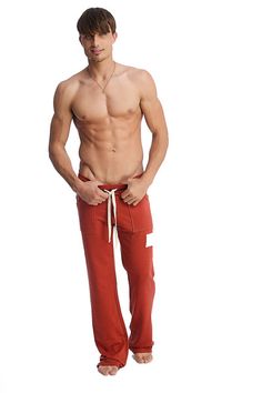 a man with no shirt is standing in red sweatpants and has his hands on his hips