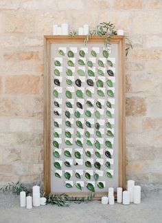 a wooden frame with some plants and candles in front of it on the ground next to a brick wall