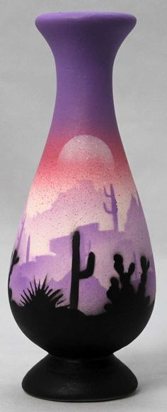 a purple and black vase sitting on top of a white table next to a cactus