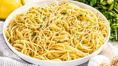 a white bowl filled with pasta next to lemons and garlic