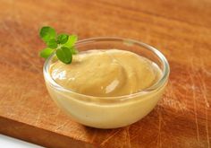 a small glass bowl filled with sauce on top of a wooden cutting board next to a knife