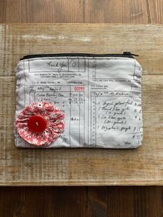 a small bag with a red flower on it sitting on top of a wooden table